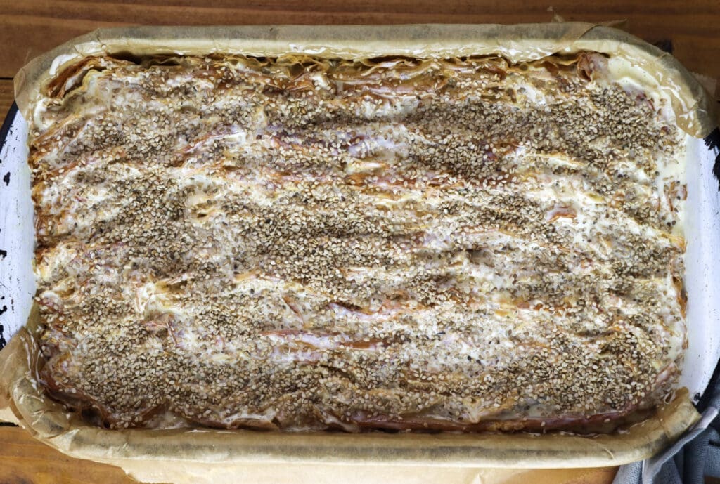 Baking the pie by chicken of the woods pie recipe - topping the phyllo sheets with sour cream and eggs, and sesame seeds on top.